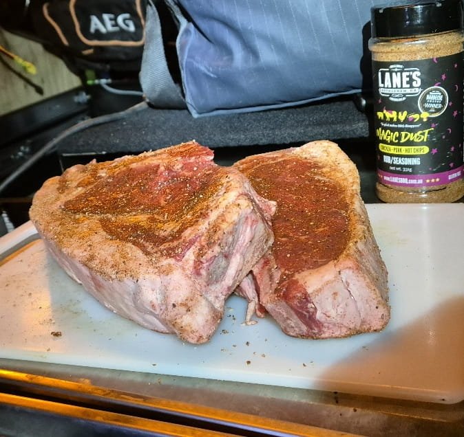 Two thick raw beef rib eye steaks rubbed with seasoning on a chopping board, ready to cook