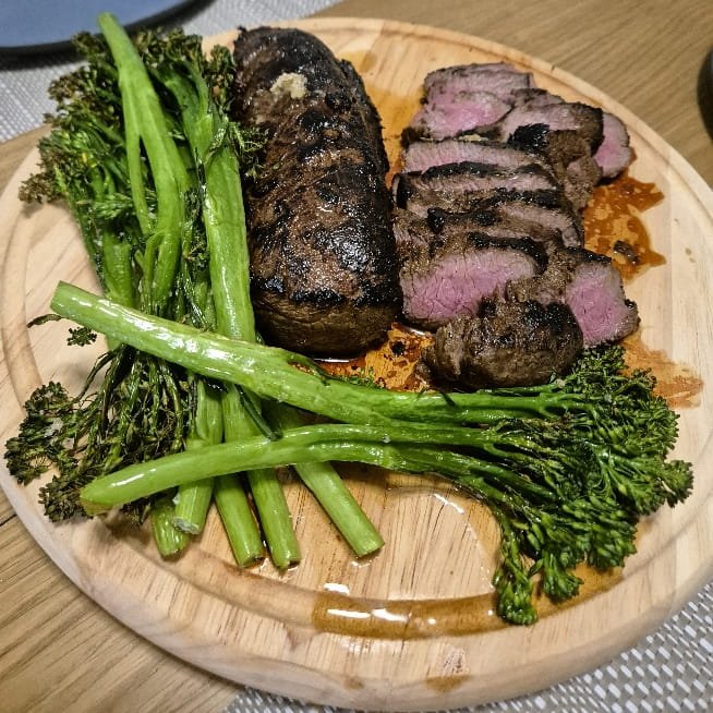 Sliced sous vide fallow deer backstrap, pink in the middle, served with broccolini on a wooden board